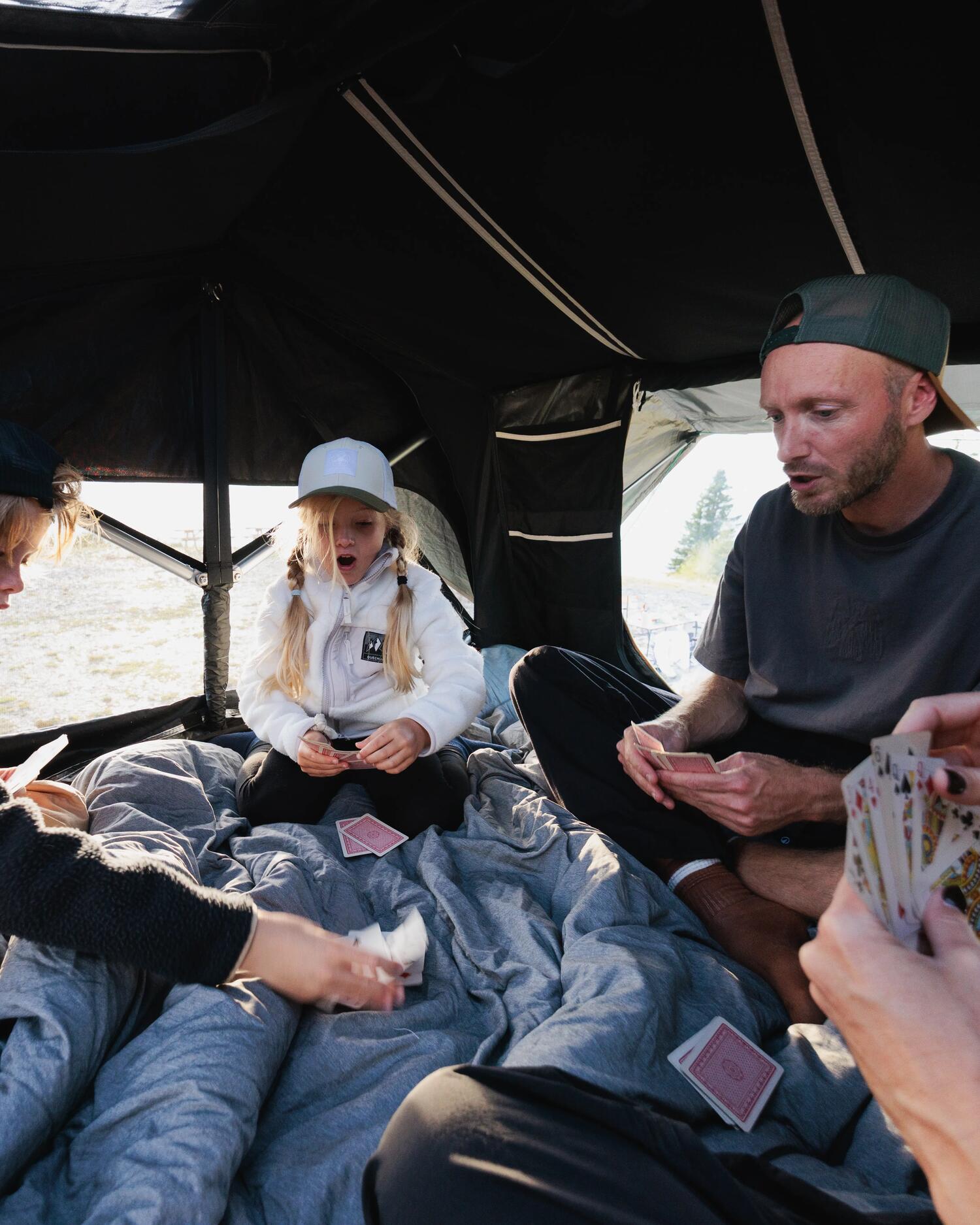 Famille assise sur le matelas de la tente de toit 500 4P, partie de cartes