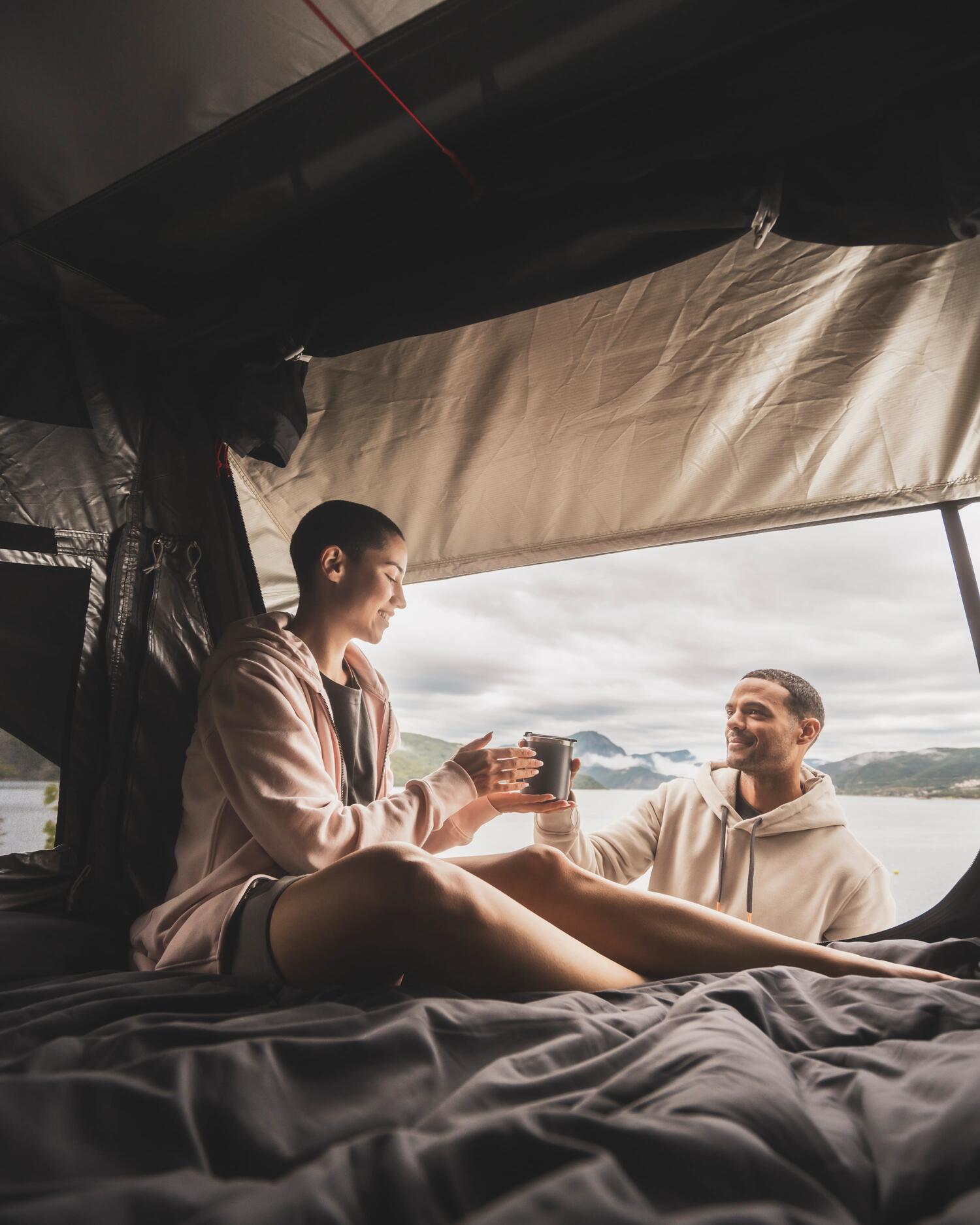 Couple assis dans la tente de toit Quechua x NaïtUp, vue sur un lac