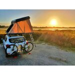 Tente de toit NaïtUp ouverte sur un SUV blanc au coucher du soleil, vélo à larrière
