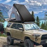 Tente triangulaire à toile grise ouverte sur un 4x4 beige au bord dun lac de montagne