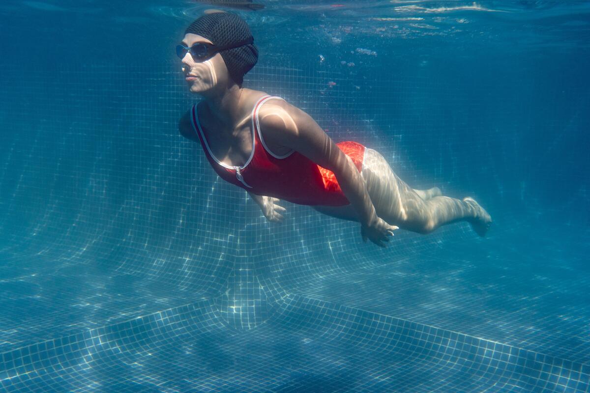 Nageuse en bonnet et lunettes sous l'eau d'une piscine