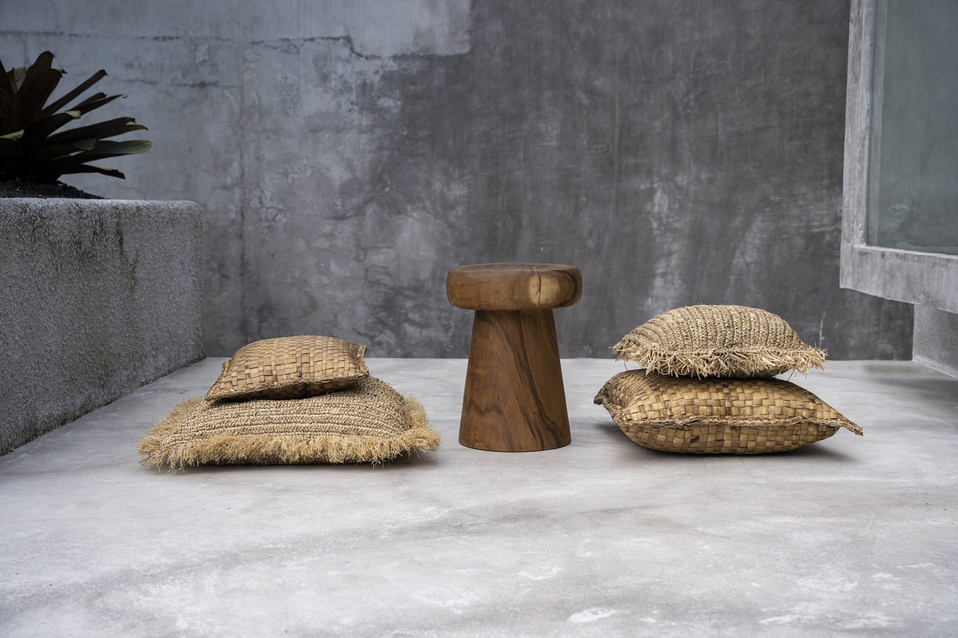 Plusieurs coussins carrés beige à côté dun tabouret en bois sur fond gris