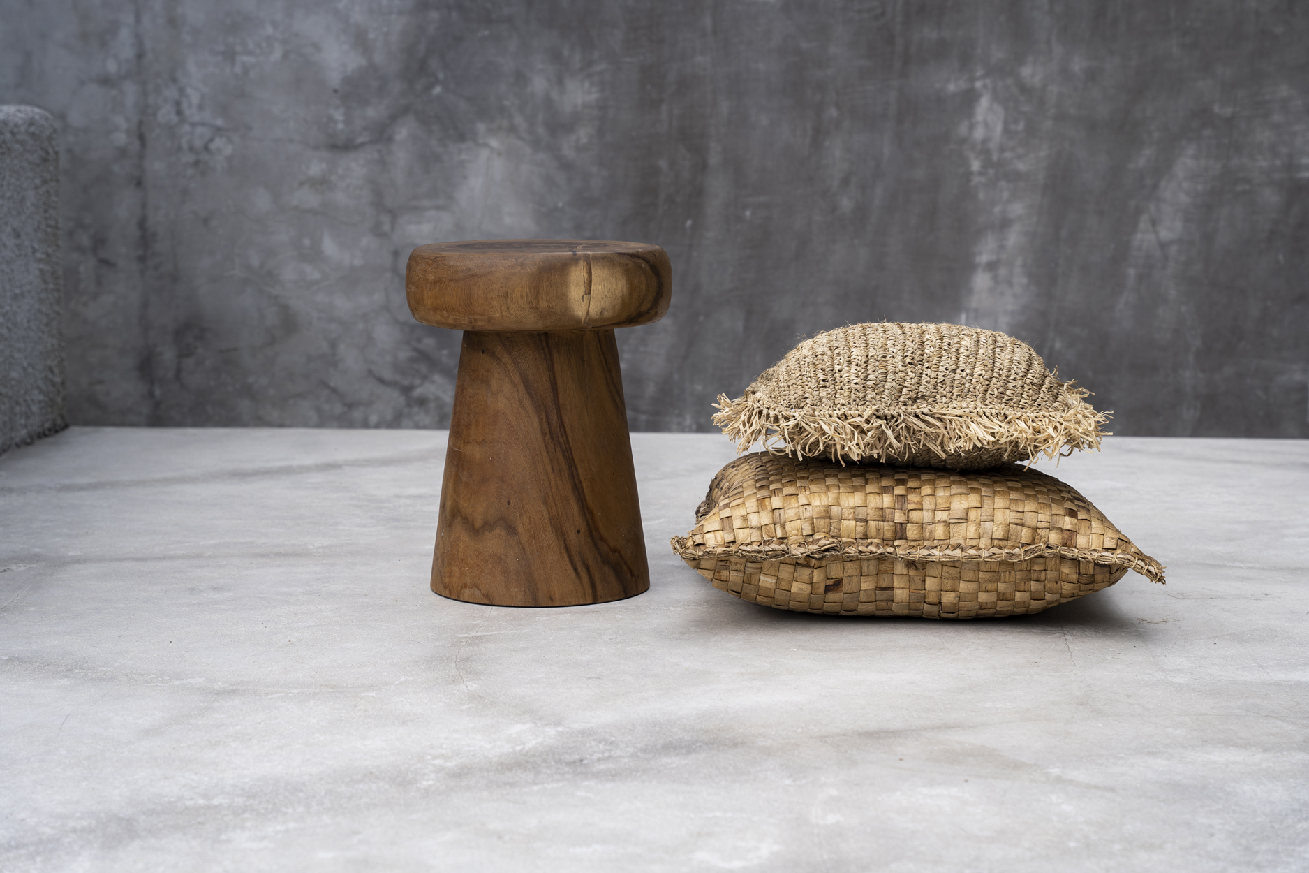 Deux coussins carrés marrons et beiges en jacinthe deau et raphia à côté dun tabouret sur fond gris