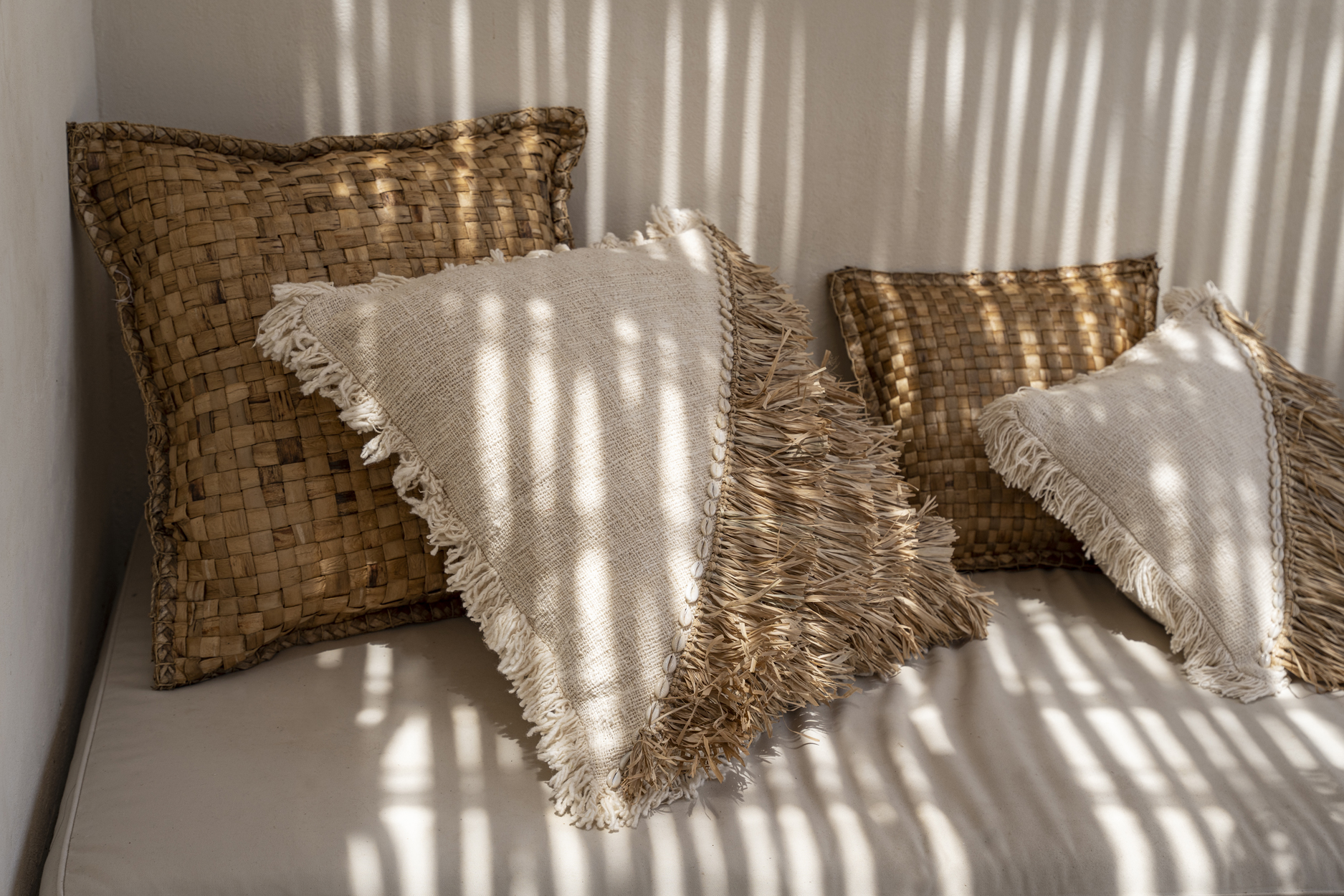 Quatre coussins carrés marrons et beiges naturels en jacinthe deau sur une banquette extérieur