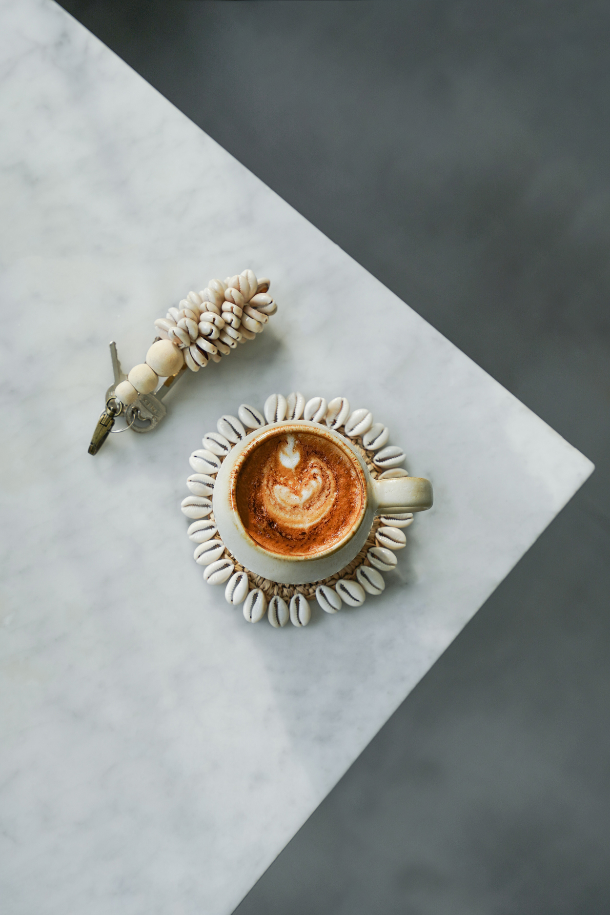 Tasse à café ronde et beige cascais en céramique sur dessous de verre raphia et coquillages sur plan de travail blanc avec porte clé coquillages bazar bizar