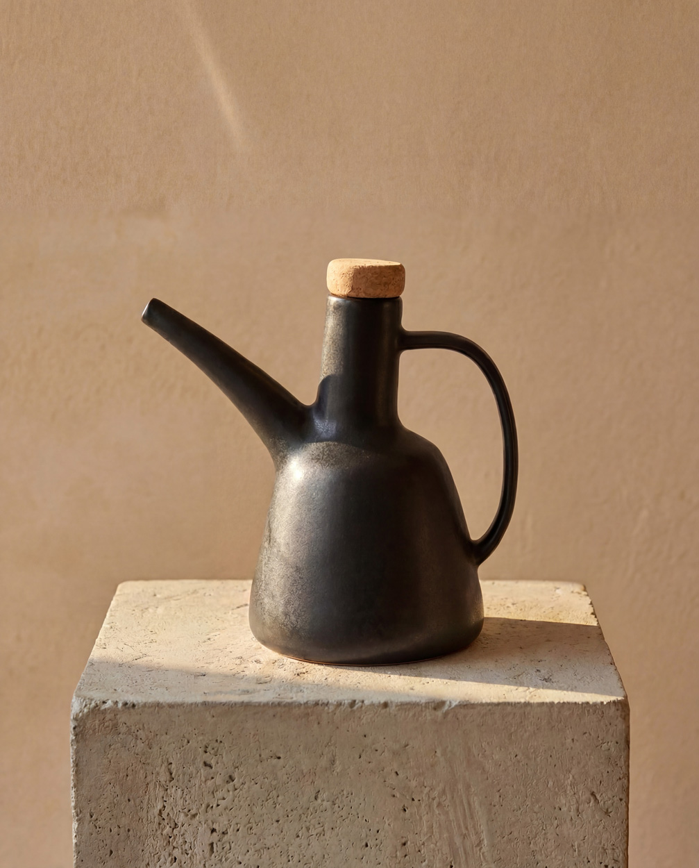 Bouteille à huile d’olive noire N°79 posée sur un socle en pierre, dans une lumière chaleureuse.