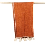 Couverture terracotta ou orange avec des broderies beiges, posée sur un support en bois