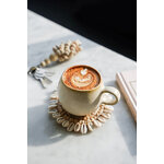 Magnifique tasse à café cascais beige et marron à la forme arrondie, posée sur un dessous de verre en raphia et coquillages