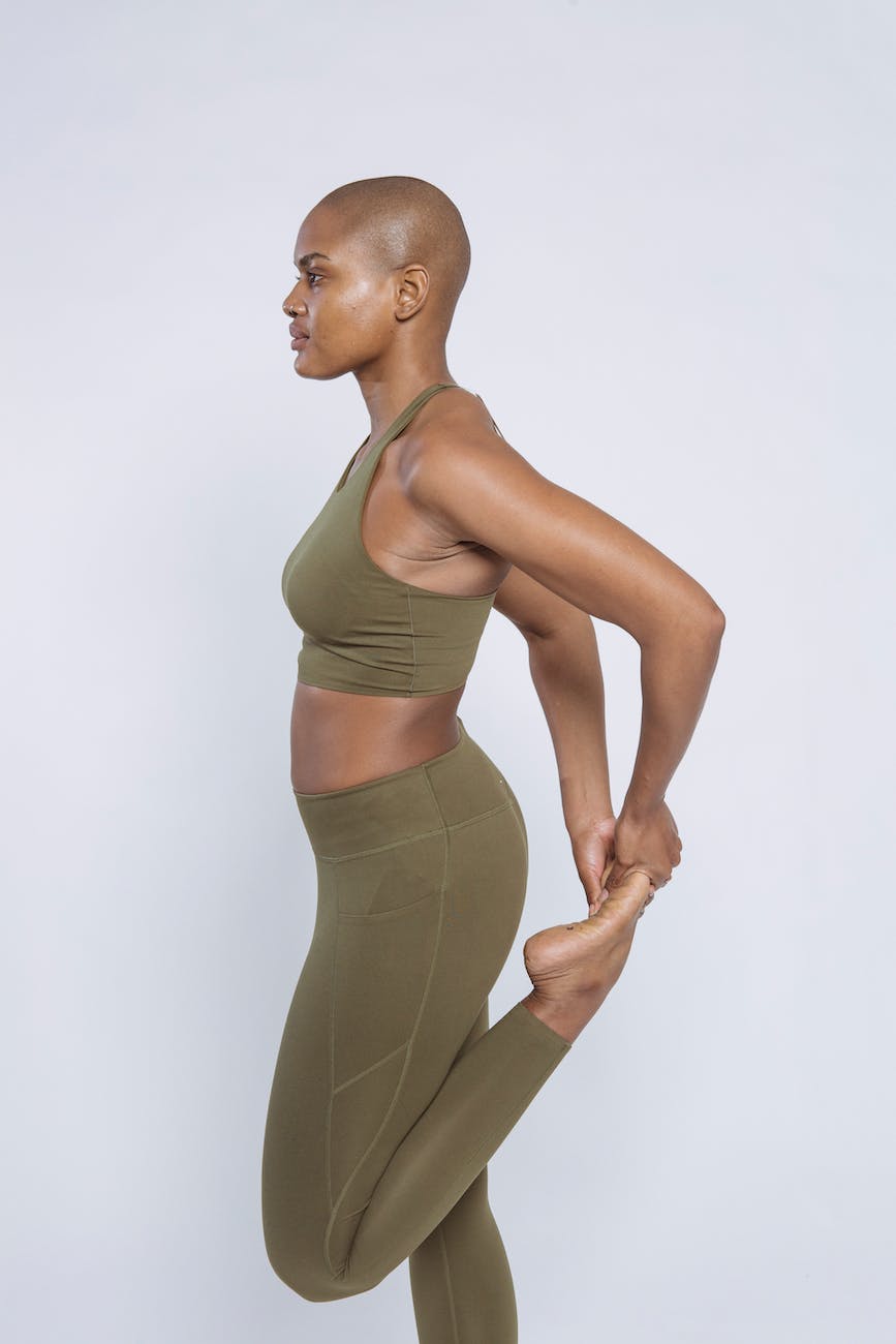side view of young sportive black female in sportswear stretching leg holding it with hand looking away against white background