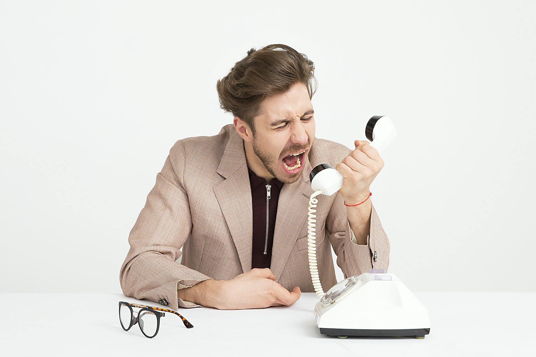 homme portant une veste de costume marron se moquant de telephone blanc