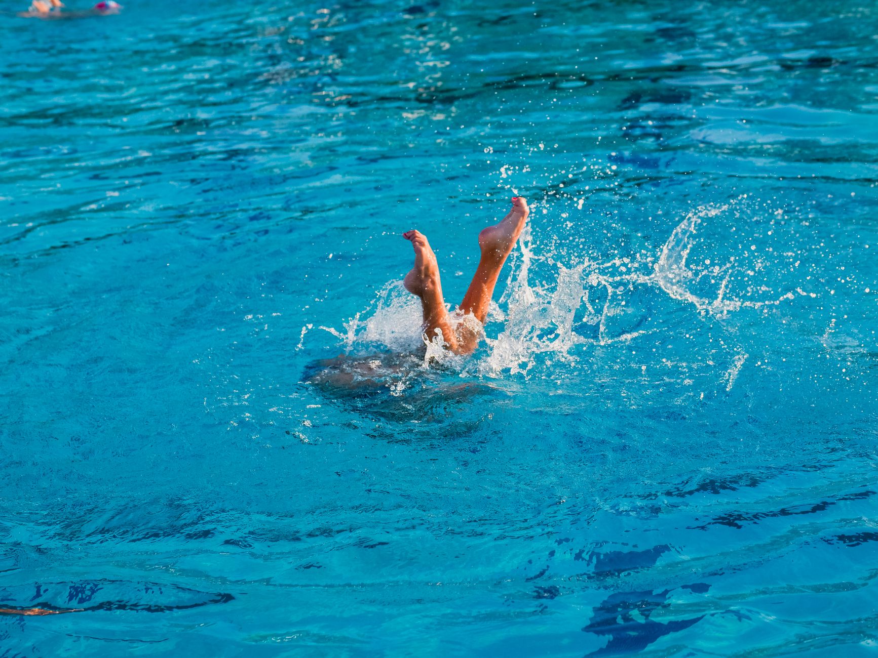 un individu plongeant dans une piscine bleue claire creant des eclaboussures