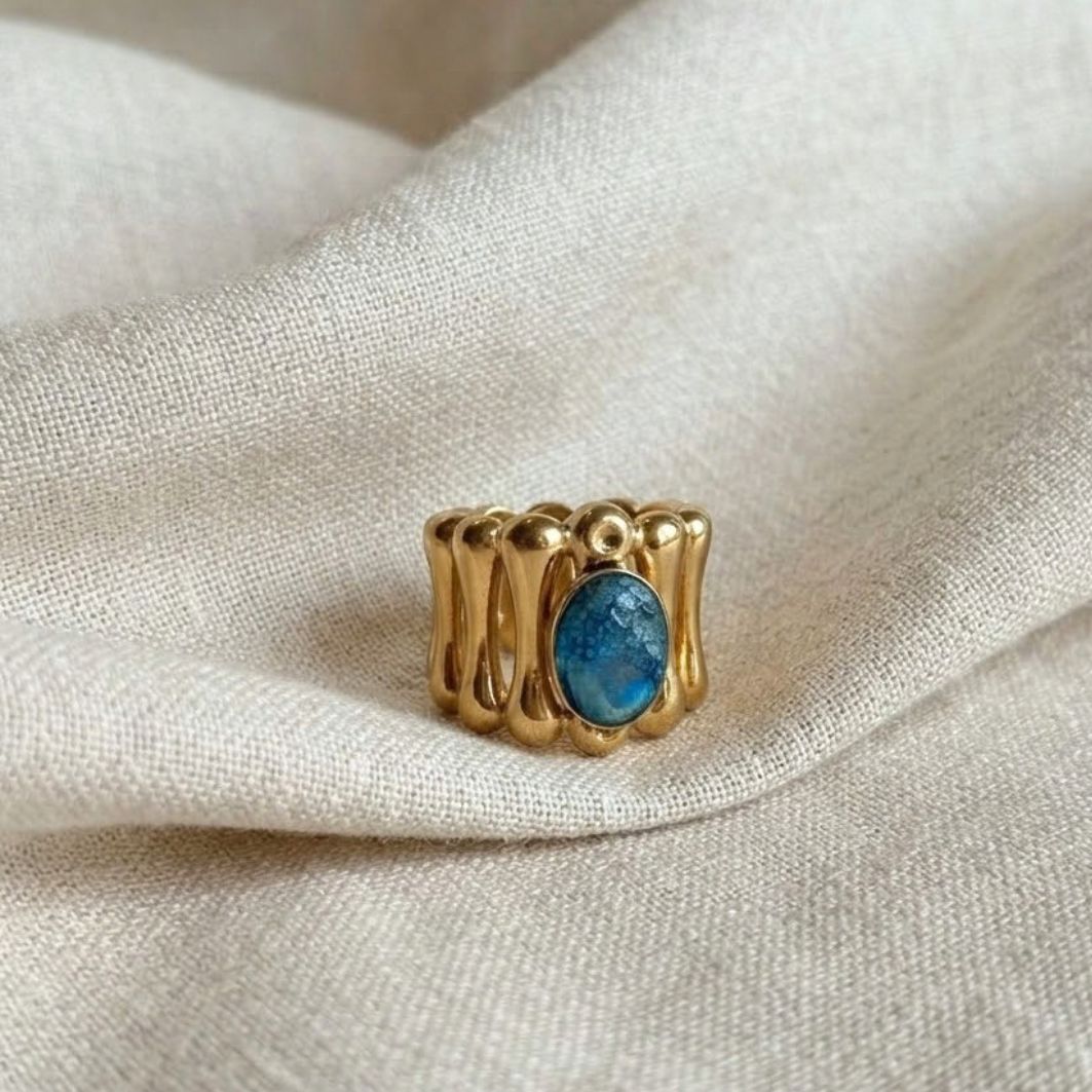 Bague Ramsès ajustable en acier doré, pierre ovale en béton irisé bleu-vert, posée sur lin