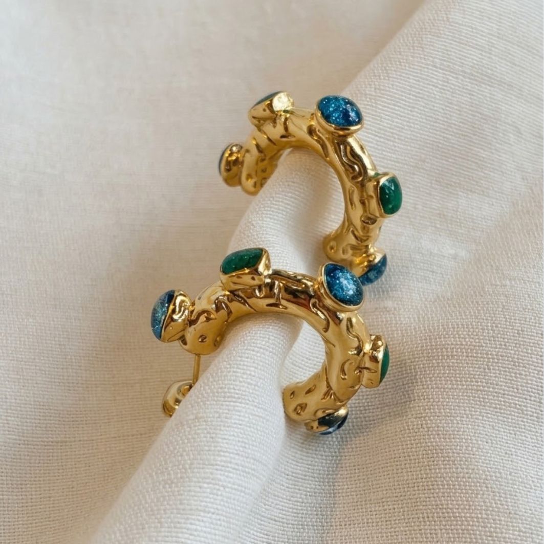 Boucles d'oreilles Néfertiti, créoles dorées martelées serties de béton irisé bleu-vert et vert, posées sur lin