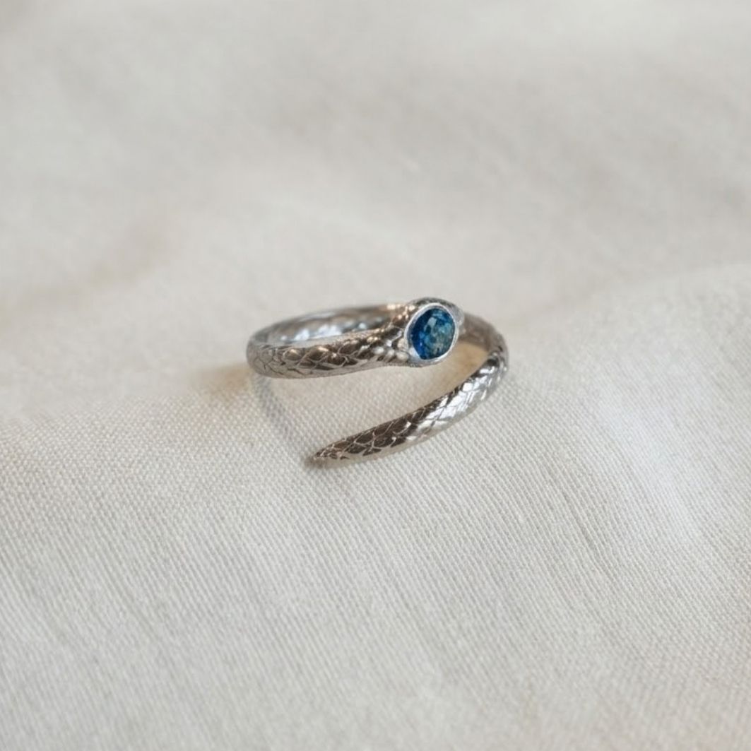 Bague Serpentine portée à la main, serpent argenté enroulé et pierre en béton irisé bleu-vert