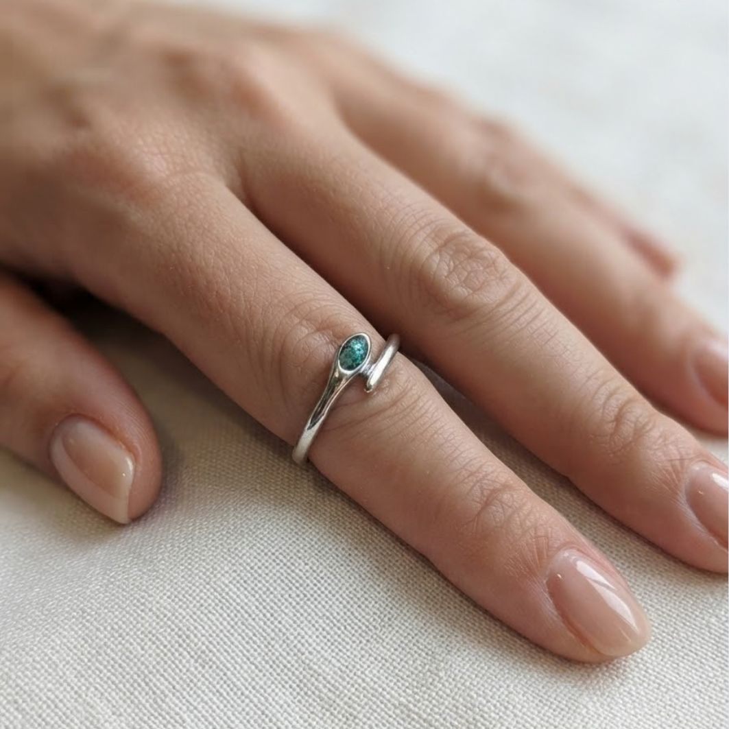 Bague Tiya portée à la main, fin serpent argenté et pierre en béton irisé bleu-vert