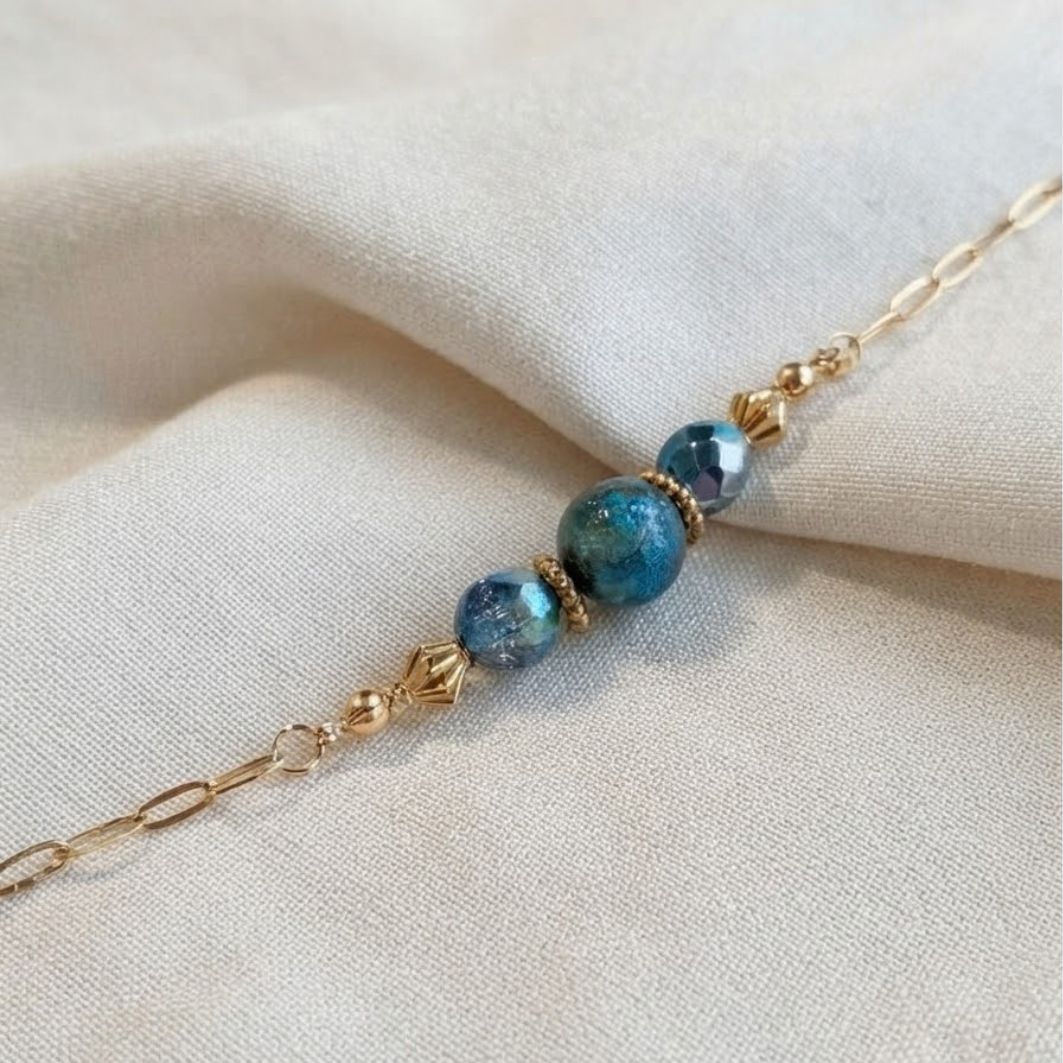 Bracelet Cristal Bleu porté au poignet, chaîne dorée et perles bleu-vert