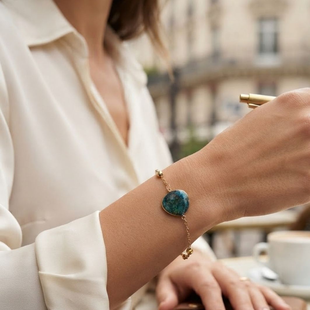 Bracelet Nour porté au poignet, chaîne fine dorée et pierre en béton irisé bleu-vert