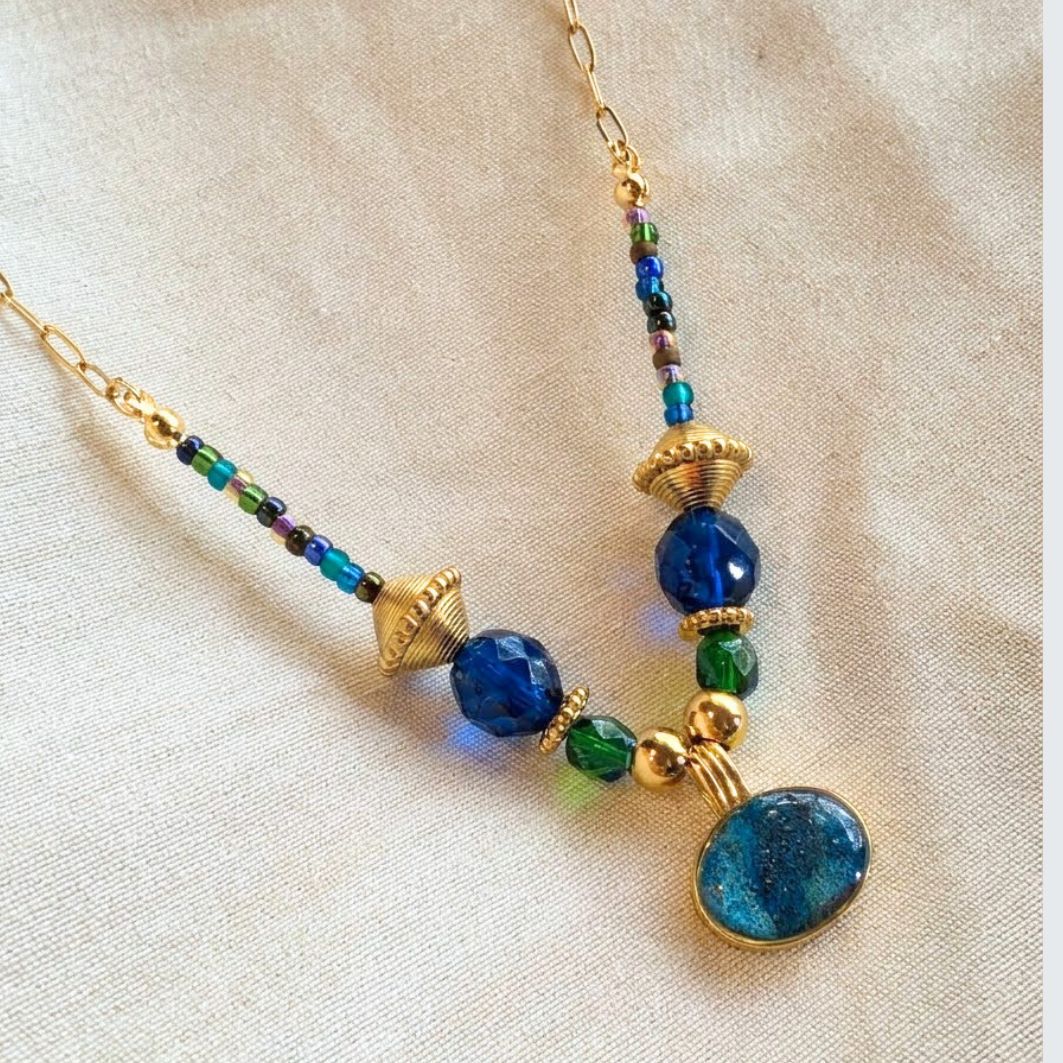 Collier Imhotep en acier doré, perles de verre et pendentif béton irisé sur lin beige