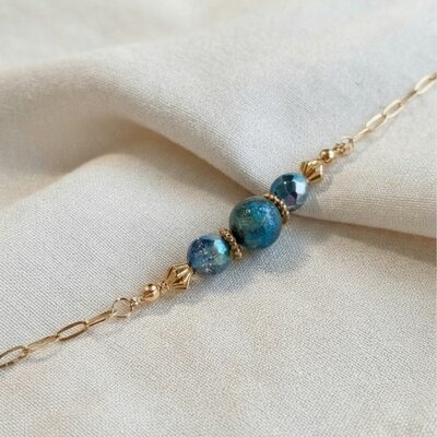 Bracelet Cristal Bleu porté au poignet, chaîne dorée et perles bleu-vert