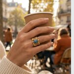 Bague Ramsès portée à la main, large anneau doré ajouré et pierre en béton irisé bleu-vert