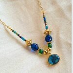 Collier Imhotep en acier doré, perles de verre et pendentif béton irisé sur lin beige