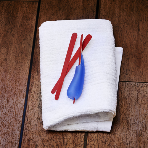 un-manche-multi-usages-bleu-avec-lime-a-ongles-introduite-dedans-pose-avec-3-limes-sur-serviette-blanche-sur-banc-de-sauna