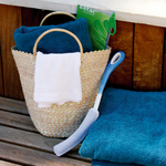 une-brosse-pour-le-corps-cylindrique-avec-manche-long-posee-a-cote-panier-en-osier-et-serviette-bleue-sur-banc-de-sauna