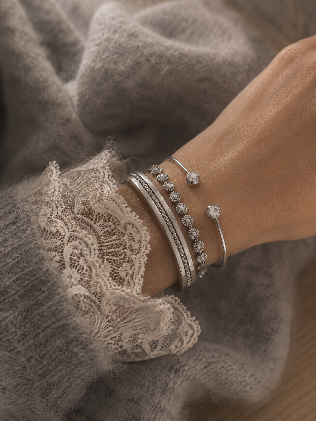 Accumulation de bracelets joncs argentés portés avec pull maille et dentelle élégante