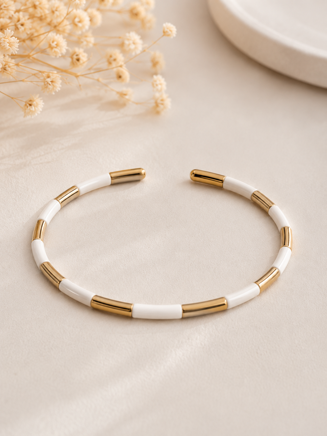 Jonc Abby blanc et doré en acier inoxydable au design minimaliste et élégant sur tissu beige texturé dans une ambiance chaleureuse et raffinée