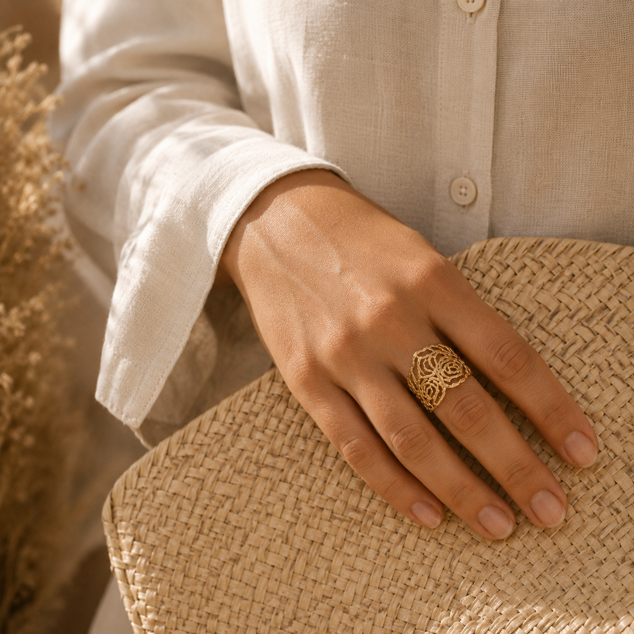 Main portant la bague Rosa dorée avec panier en osier et chemise beige – bijou femme bohème chic Bella Cosa