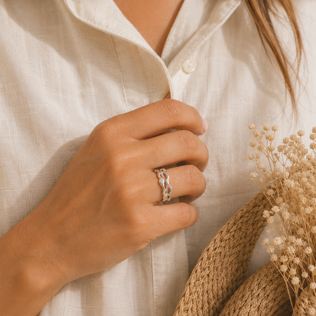 Main portant la bague Léa argentée avec chemise en lin écru et panier tressé – bijou femme élégant Bella Cosa