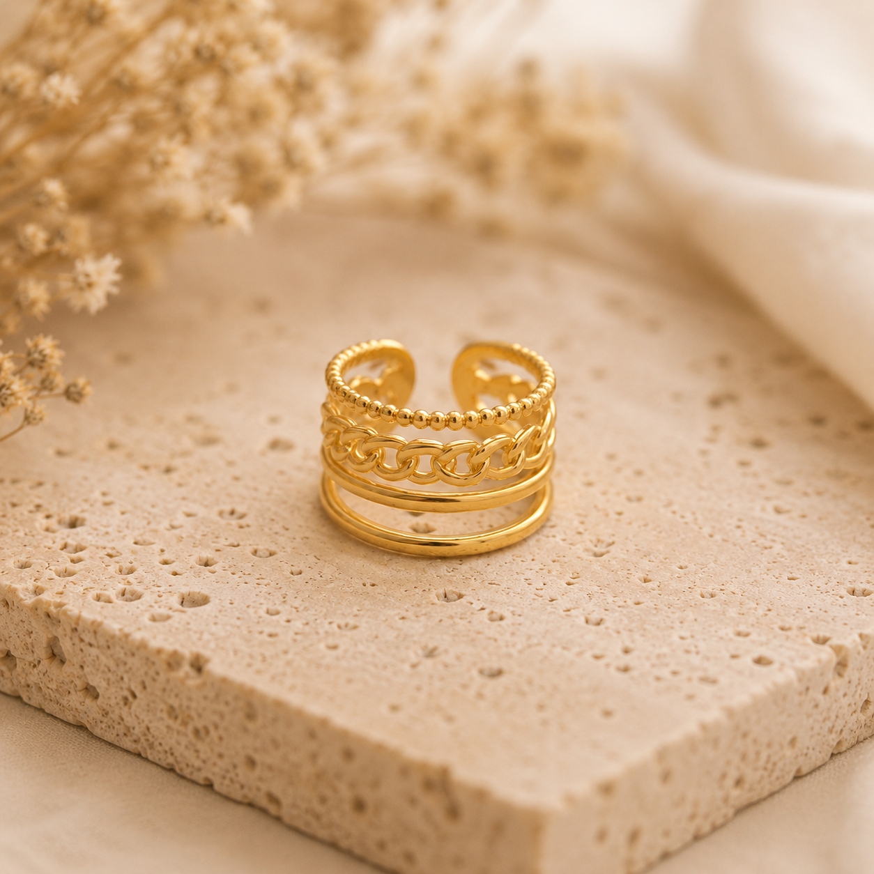 Bague Ornella dorée posée sur pierre travertin beige avec arrière-plan flouté – bague femme chic Bella Cosa