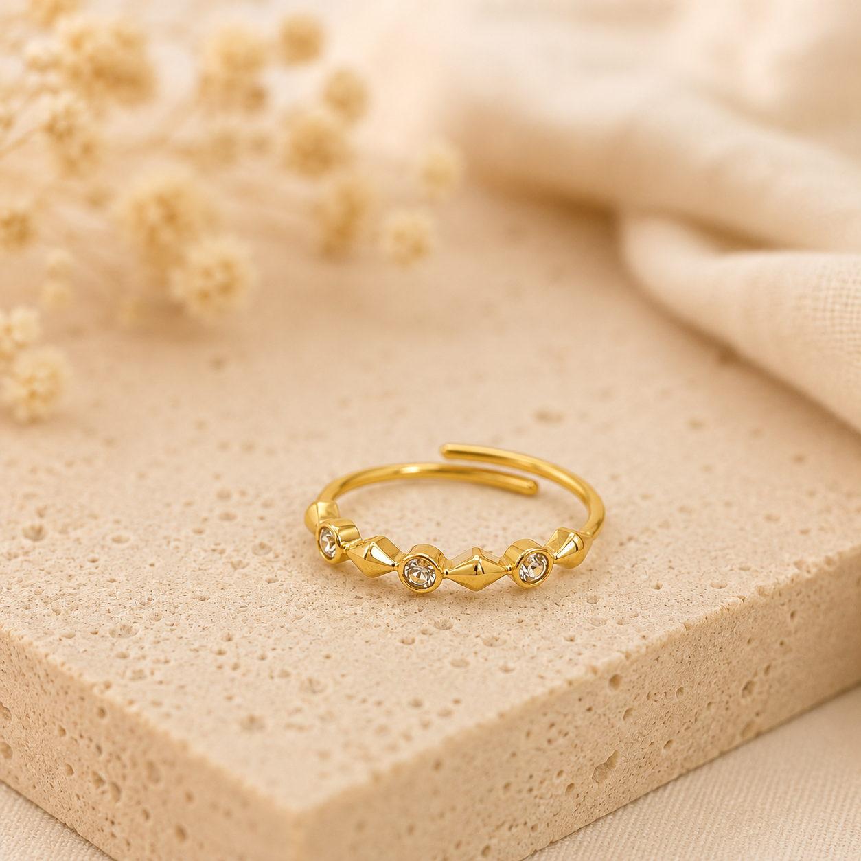 Bague Oya dorée avec cristaux posée sur pierre naturelle beige avec arrière-plan flouté – bijou femme Bella Cosa