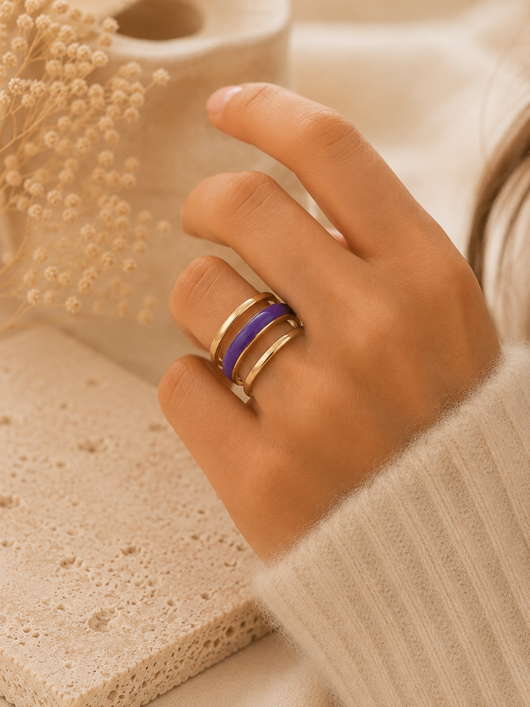 Main portant la bague Veha violette et dorée avec pull mohair beige dans une ambiance chaleureuse et élégante – bijou femme Bella Cosa