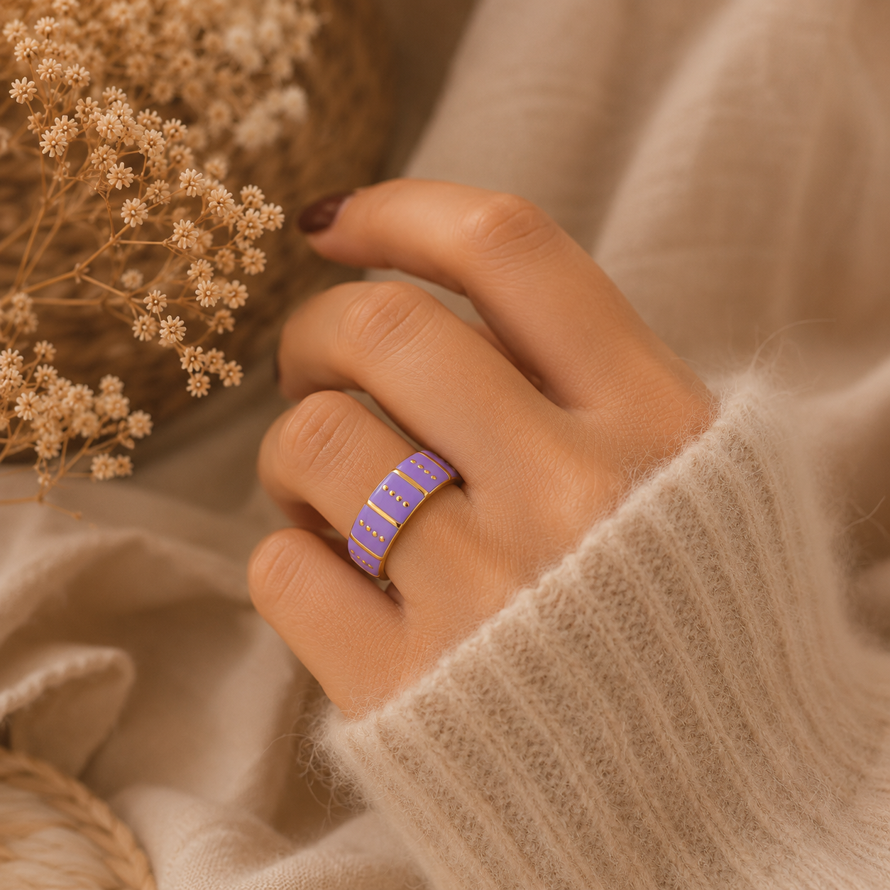 Main portant la bague Vic violette et dorée avec pull mohair beige dans une ambiance douce et élégante – bijou femme Bella Cosa