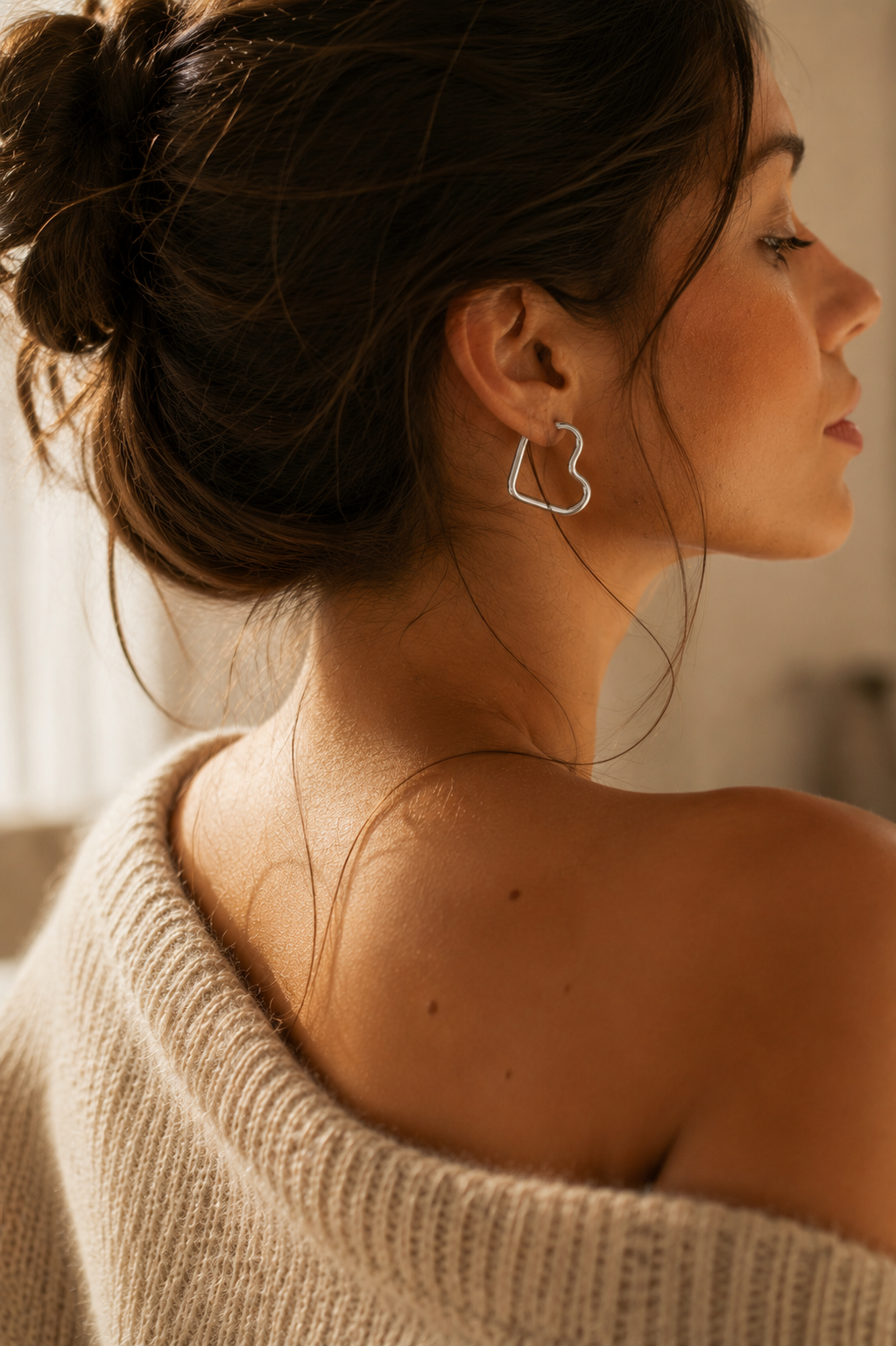 Femme brune portant les boucles d’oreilles Prya argentées en forme de cœur dans une ambiance douce et lumineuse