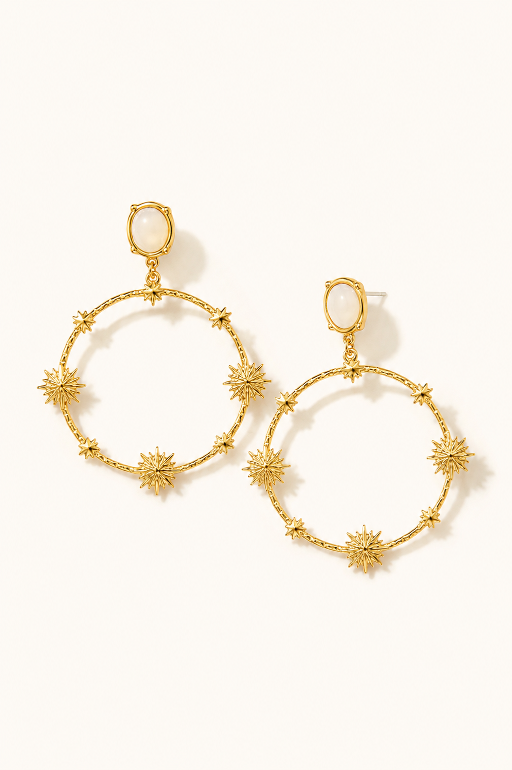 Boucles d’oreilles Alma dorées sur fond crème minimaliste style bijou élégant et lumineux