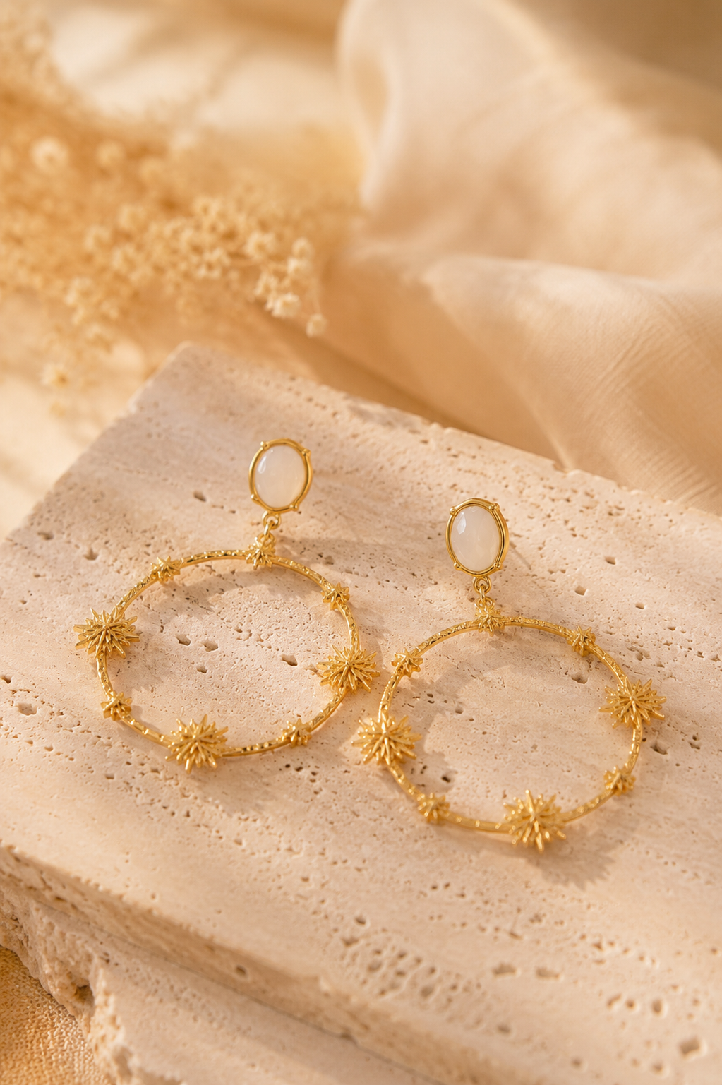Boucles d’oreilles Alma dorées posées sur travertin et lin beige lumière naturelle chaleureuse