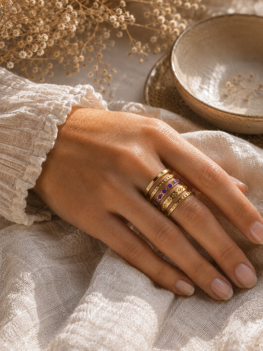 Main portant la bague Valéria dorée et violette dans une ambiance douce et naturelle aux tons beige et caramel – bijou femme Bella Cosa