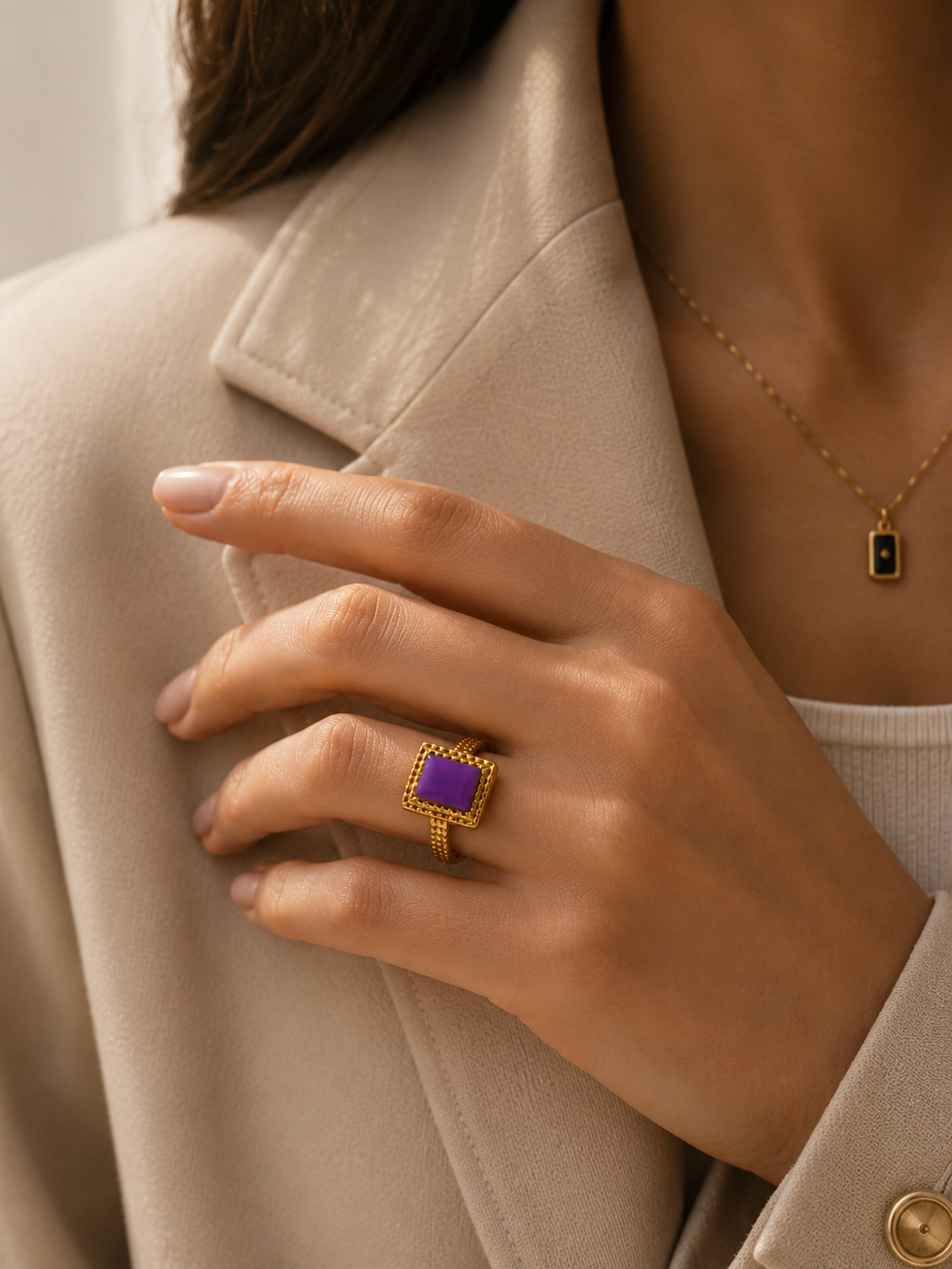Main portant la bague Vélina dorée avec pierre violette dans une ambiance chic et moderne aux tons beige et doré – bijou femme Bella Cosa