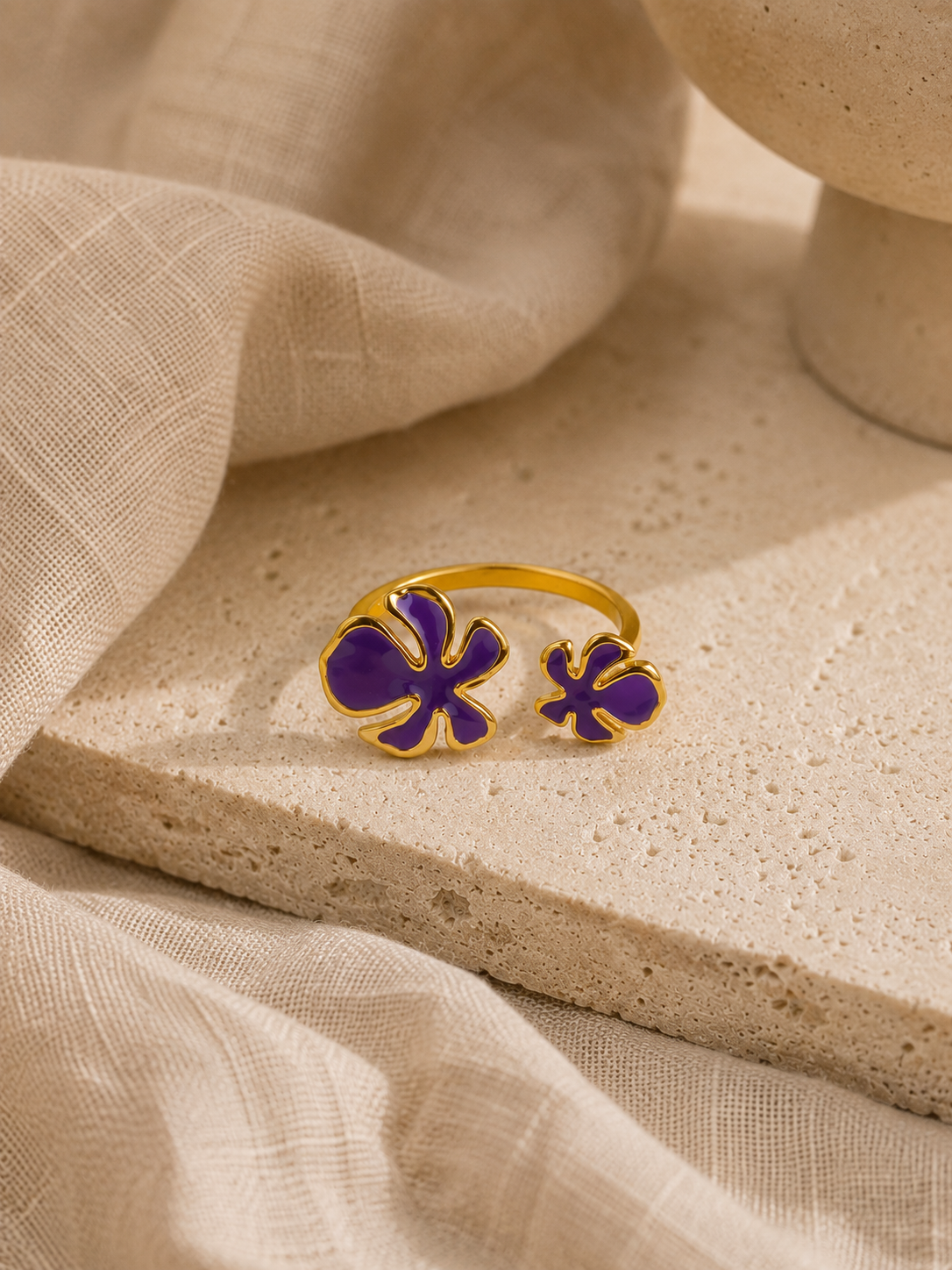 Bague Vélina dorée et violette posée sur travertin beige et tissu naturel dans une ambiance chaleureuse et raffinée – Bella Cosa