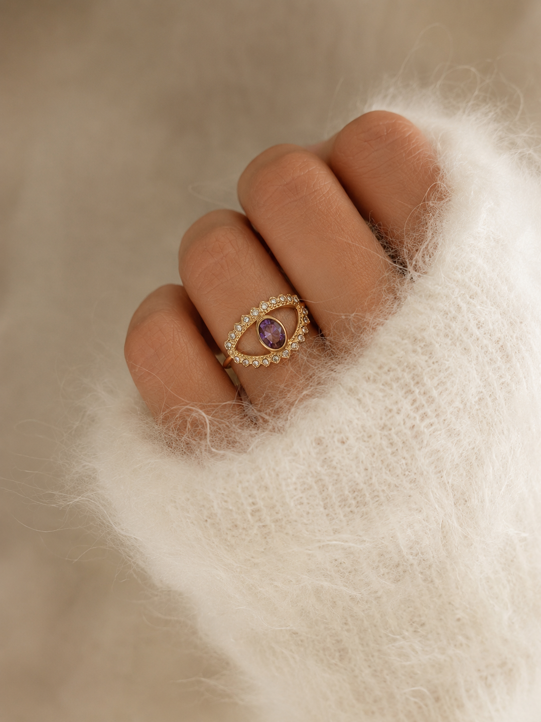 Main portant la bague Victoria dorée avec pierre violette sur pull mohair blanc tout doux dans une ambiance cosy et élégante – bijou femme Bella Cosa