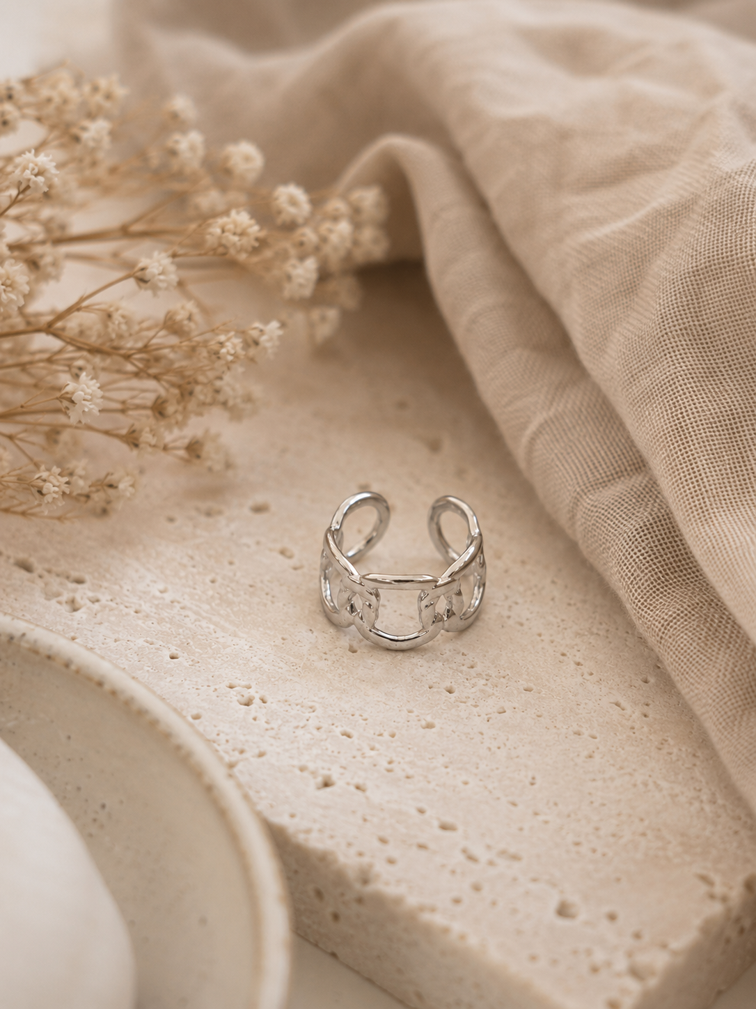 Bague Pia argentée posée sur travertin beige et tissu naturel dans une ambiance douce et chaleureuse – Bella Cosa