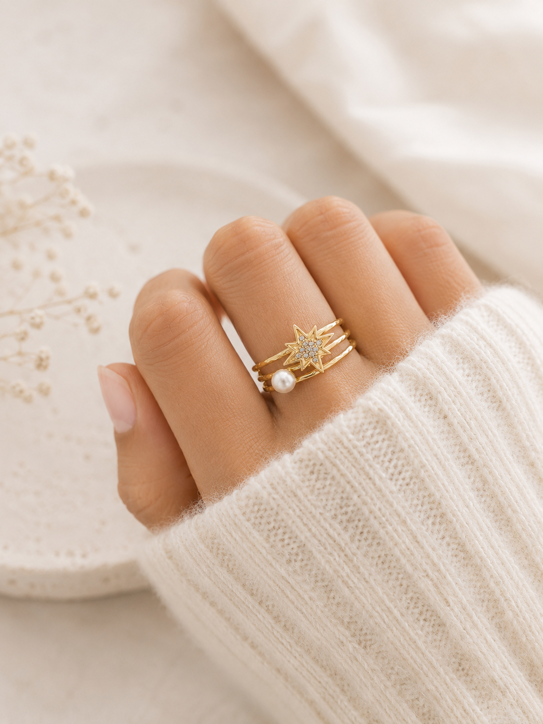 Bague Anna dorée avec étoile scintillante et perle posée sur travertin beige et lin naturel dans une ambiance douce et chaleureuse – Bella Cosa