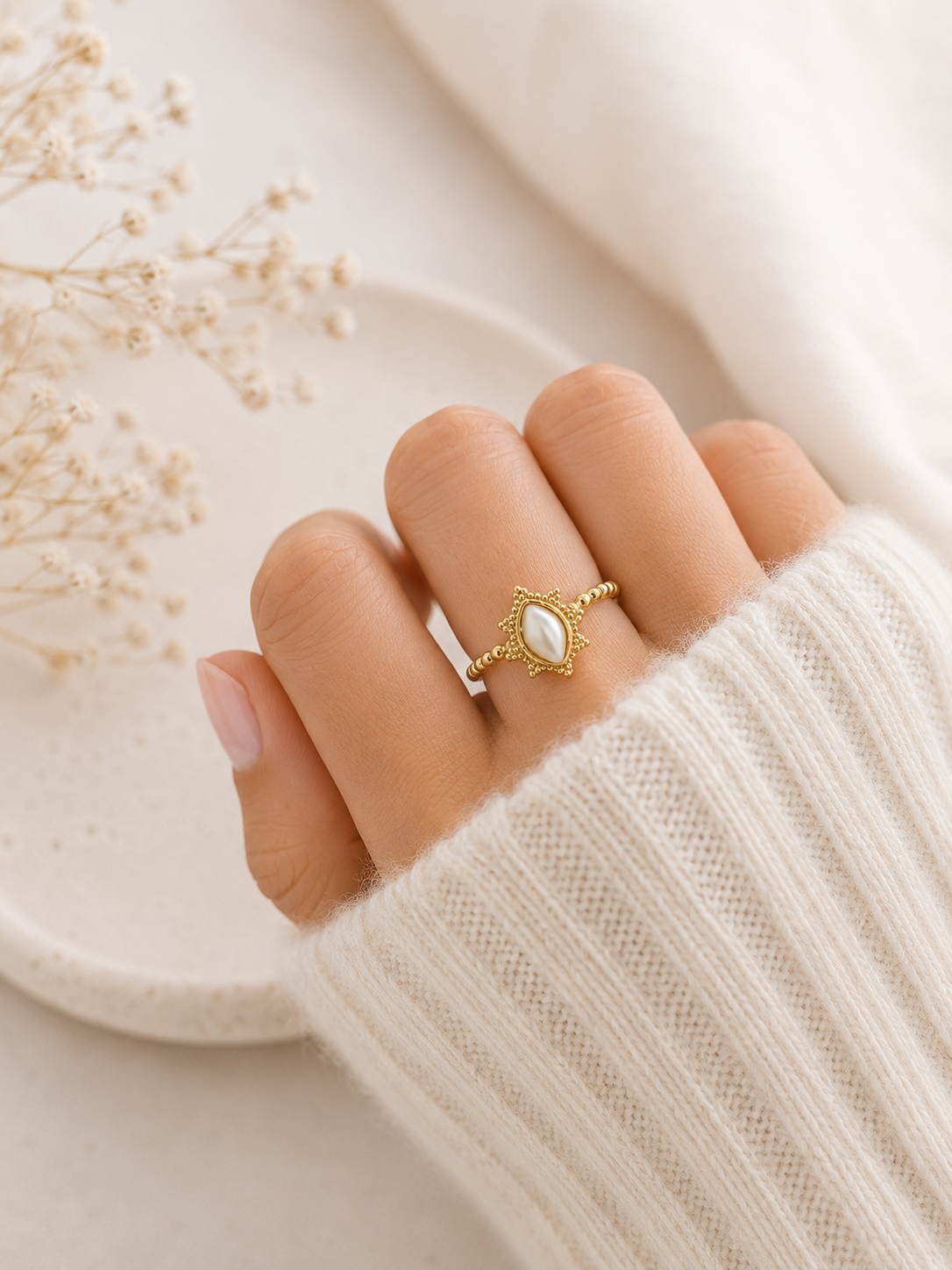 Main portant la bague Alba dorée avec pierre nacrée blanche sur pull mohair crème dans une ambiance cosy et naturelle – bijou femme Bella Cosa