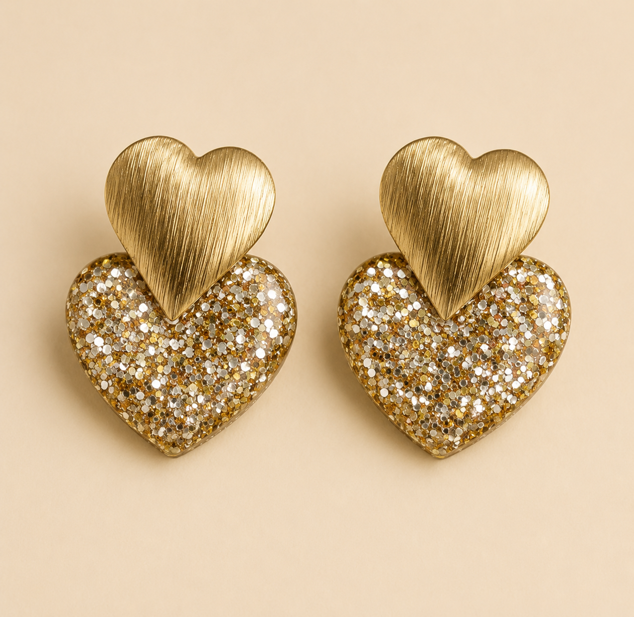 Boucles d’oreilles Caroline dorées cœur pailleté sur fond beige clair style bijou élégant et lumineux