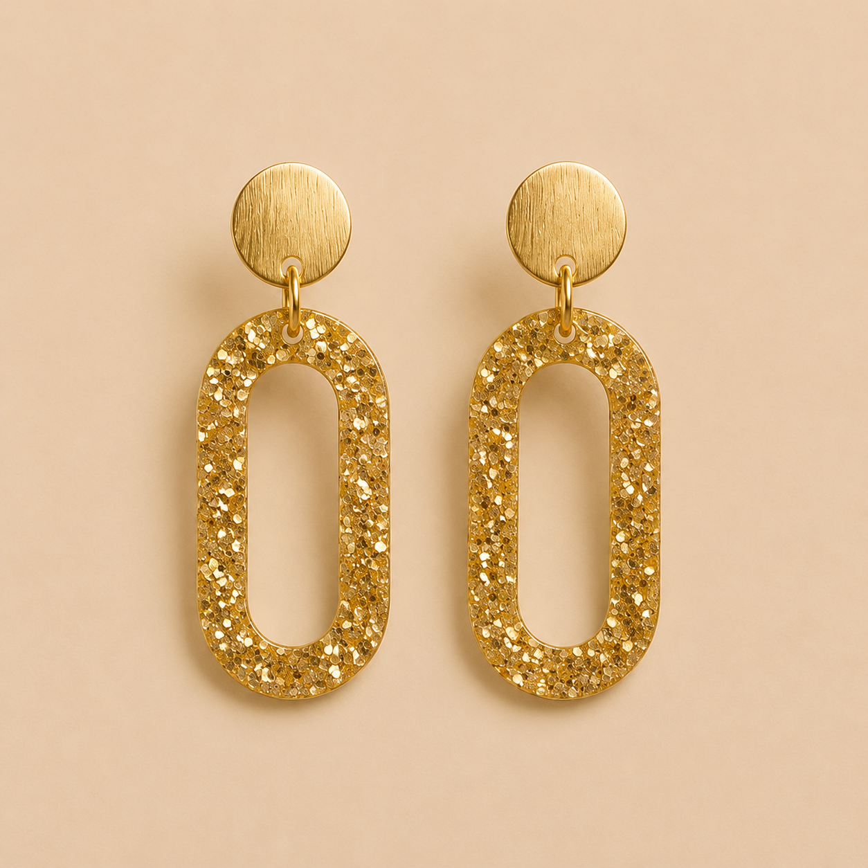 Boucles d’oreilles Clémentine dorées en résine pailletée sur fond beige élégant