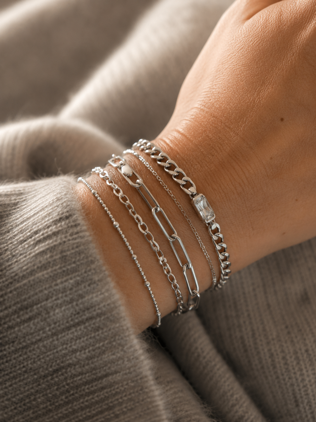 Bracelet Gena argenté style gourmette avec pierre facettée lumineuse porté en accumulation sur un poignet féminin