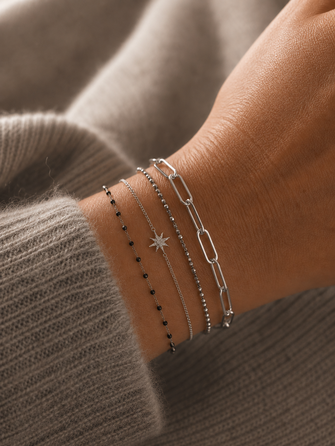 Bracelet Ginnie argenté à maille trombone porté sur un poignet féminin avec accumulation de bracelets fins argentés