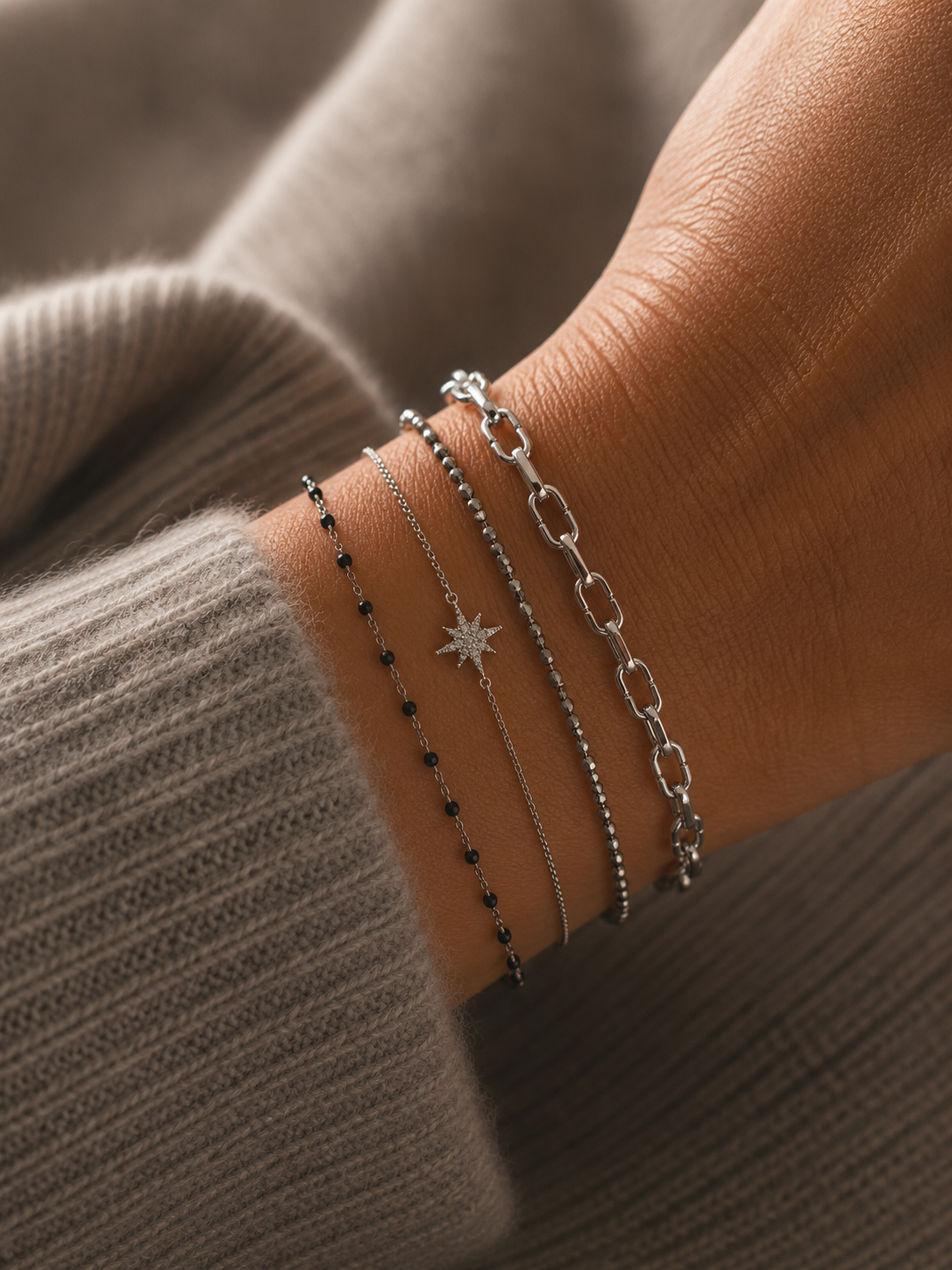 Bracelet Gaya argenté à mailles géométriques porté sur un poignet féminin avec accumulation de bracelets fins argentés